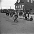 Deltager i Ungdommens Cykelløb suser forbi Saralyst Købmandsforretning ved hjørnet af Rosenvangs Allé og L.A. Rings Vej. Fotograf Ib Hansen, 1951, Aarhus Stadsarkiv